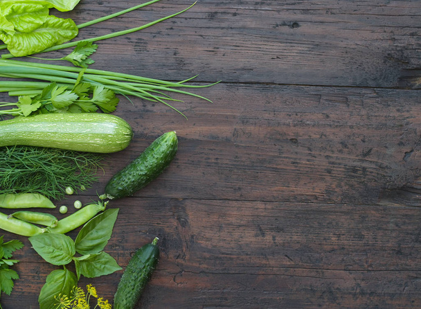 Green vegetables on wooden background (peas, parsley, basil, cucumber, dill, onion ,salad) - Photo, image