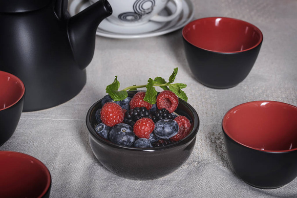 Articles pour le thé sur la table, tasses noires et rouges avec des baies noir-rouge
 - Photo, image