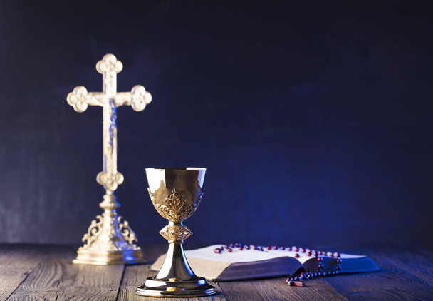 ローマ カトリック教会のテーマです。十字架、聖書、ロザリオ、茶色の木製のテーブルに黄金の杯. - 写真・画像