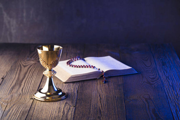 Tema Iglesia Católica Romana. Santa Biblia, rosario y cáliz dorado sobre mesa de madera marrón
. - Foto, Imagen