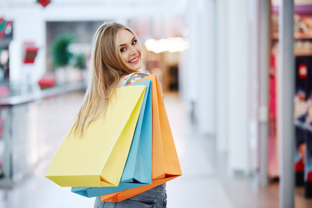 όμορφη ξανθιά νεαρή γυναίκα που ποζάρει με πολύχρωμες τσάντες για ψώνια στο εμπορικό κέντρο - Φωτογραφία, εικόνα