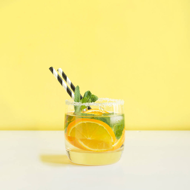 Fresh summer fruits water or lemonade with lemon, orange and mint on yellow background. Close up. - Photo, Image