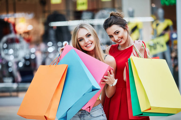Gelukkig jonge vrouwen met kleurrijke boodschappentassen bij winkelcentrum - Foto, afbeelding