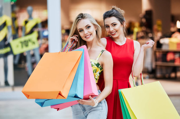 happy young women with colorful shopping bags at shopping mall - Foto, Imagen