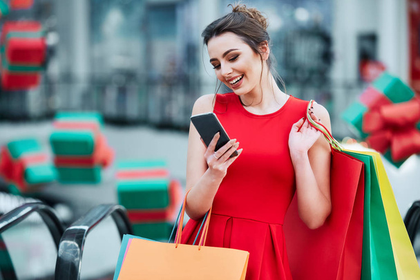 belle brune jeune femme avec des sacs à provisions colorés en utilisant le téléphone mobile, concept de magasinage en ligne
 - Photo, image