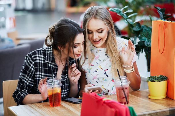 mulheres jovens atraentes com sacos de compras coloridos usando telefones celulares no café
 - Foto, Imagem