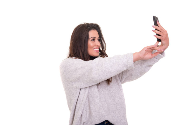 Joyeux jeune femme prenant la photographie autoportrait par téléphone intelligent sur fond blanc
. - Photo, image