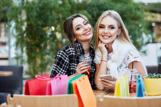 happy female friends posing with colorful shopping bags in outdoor cafe, summer shopping concept  - Photo, Image
