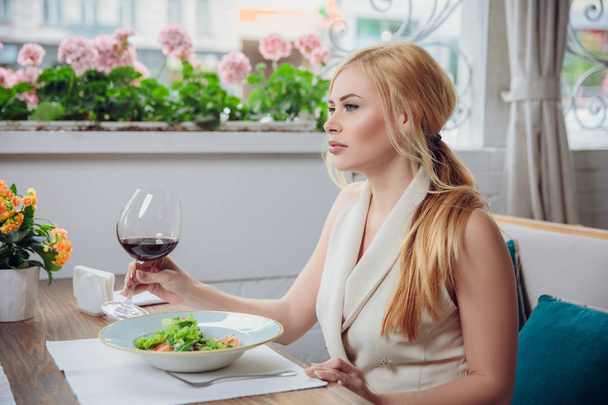 Молодая блондинка пьет красное вино в ресторане на открытом воздухе
 - Фото, изображение