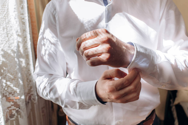 elegante noivo vestindo camisa com botões de punho e gravata na janela. elegante rico noivo se preparando pela manhã
 - Foto, Imagem