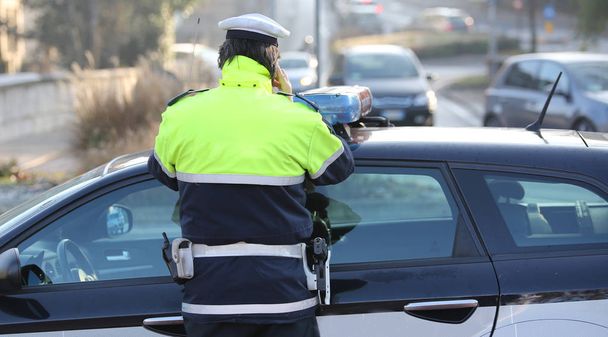 Italiaanse politieagent met een fosforescerende jas tijdens het gesprek op de telefoon - Foto, afbeelding