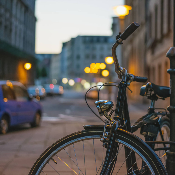 Bicicleta em estilo retro presa a um poste no escuro em uma rua em uma cidade europeia
 - Foto, Imagem