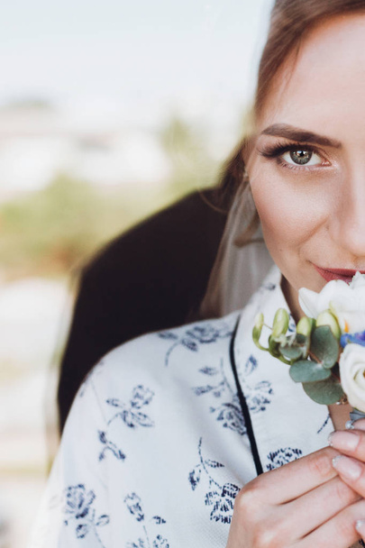 美しく幸せな花嫁のウィンドウでシルクのローブで立っているブートニ エールを保持 - 写真・画像