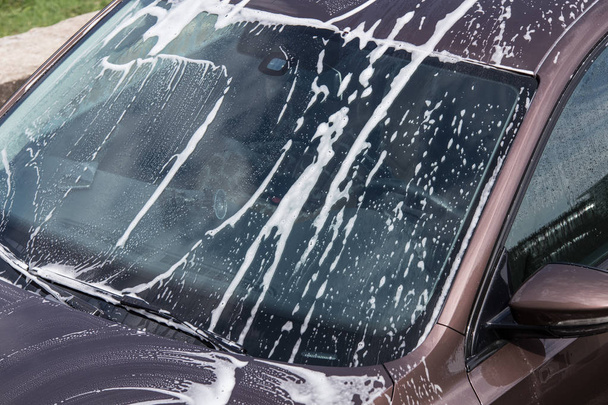 Car front window with washing foam. Car washing service background. - Foto, afbeelding