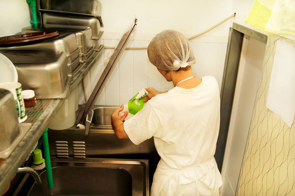 Köchin und Arbeiterin arbeitet in einer Eisfabrik und gießt pasteurisierte Milch und kocht Mischmilch in einer Pasteurisierungsmaschine, die die Grundlage für die Eiscremeproduktion vorbereitet. Zubereitung von Eis. - Foto, Bild