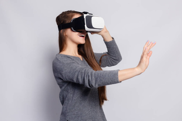 technology, virtual reality, entertainment and people concept - happy young woman with virtual reality headset or 3d glasses. Woman with virtual reality goggles. Studio shot, gray background - Φωτογραφία, εικόνα