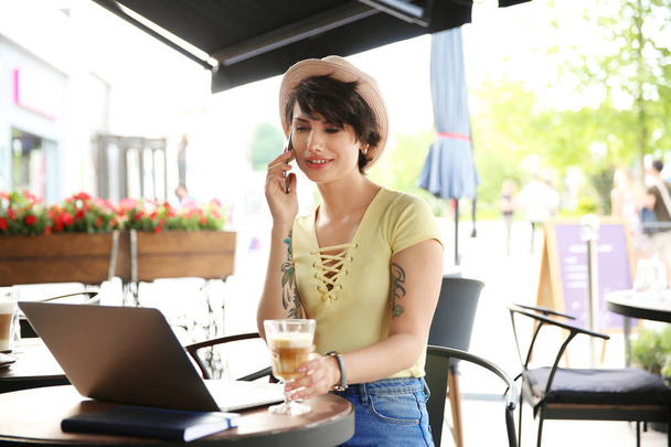 Young woman talking on phone while working with laptop at desk in cafe - Foto, imagen