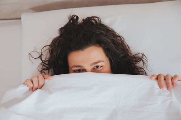 κοντινό πλάνο του μια νεαρή γυναίκα που κρύβονται κάτω από τα φύλλα στο κρεβάτι της - Φωτογραφία, εικόνα