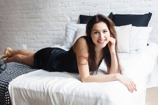 people, beauty, depilation, epilation and bodycare concept - beautiful woman with bare legs sitting on bed at home bedroom. happy young woman smiling in bed. - Fotó, kép