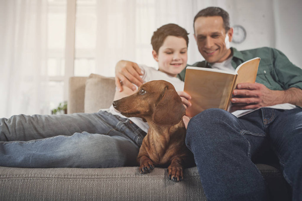 Father and son reading book near puppy - Zdjęcie, obraz
