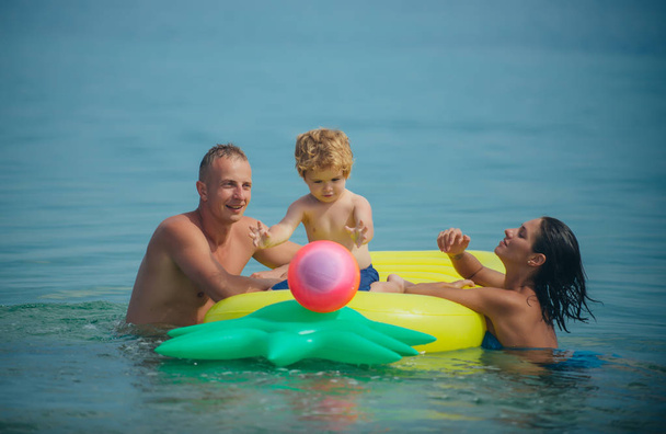 Summer vacation and travel to ocean. Father and mother with son play ball in water. Pineapple inflatable or air mattress. Maldives or Miami beach activity joy. Happy family couple on Caribbean sea. - Φωτογραφία, εικόνα