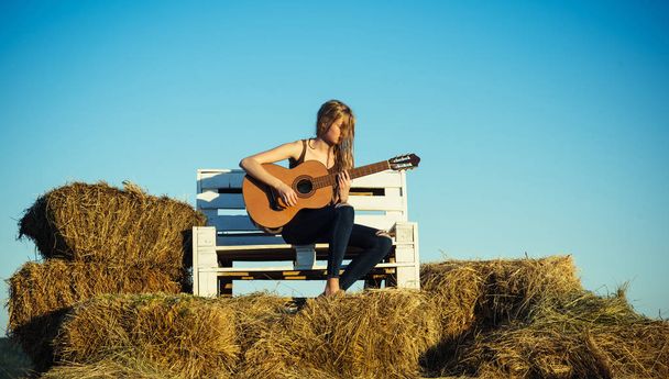 Guitar player on wooden bench on blue sky. Guitar performer hold string instrument on sunny nature. - Foto, Imagen