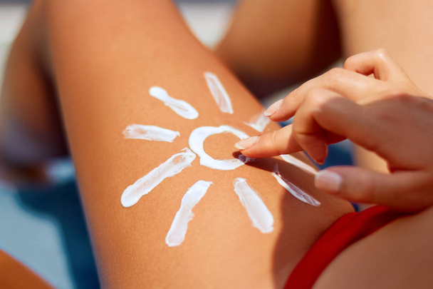 Protection solaire. Femme utilisant la crème solaire à la plage sous forme de soleil sur la jambe
 - Photo, image