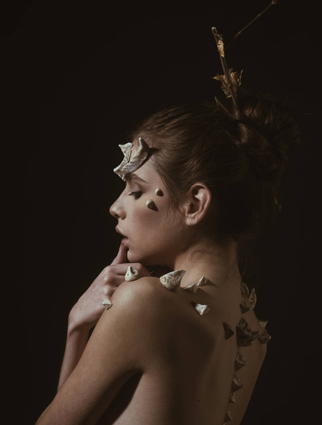 Portrait of brunette girl with fictional make-up and thorns on face, fragile spirit of nature, tenderness concept. Side with woman with spikes on back and shoulders isolated on black background. - Foto, afbeelding