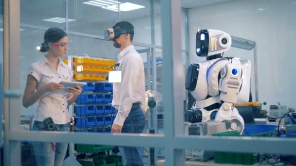 Robô semelhante ao humano está copiando movimentos de um trabalhador de laboratório masculino sob supervisão
 - Filmagem, Vídeo