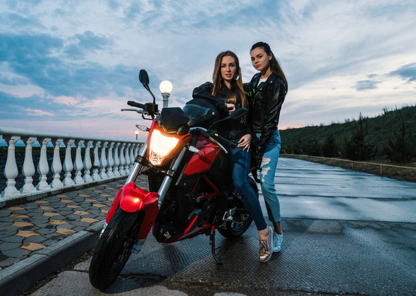 zwei Motorradmädchen in Lederjacken auf einem schwarz-roten Sportmotorrad - Foto, Bild