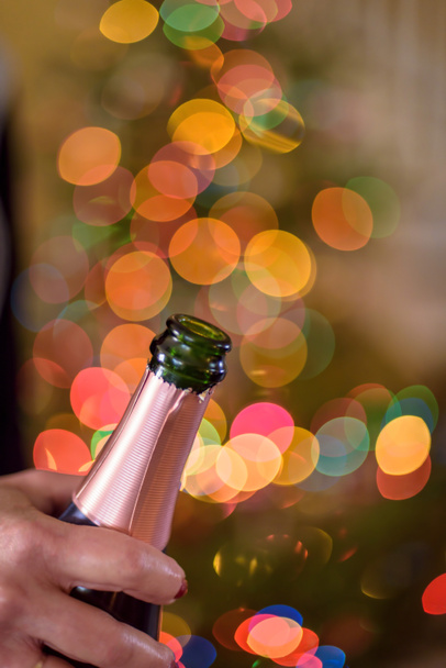 Close-up van een vrouw met een champagne fles voor bokeh Kerstverlichting op New Years Eve - Foto, afbeelding