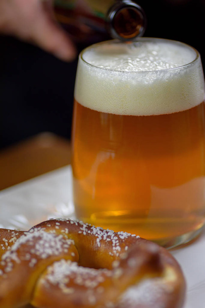 наливая пиво в большую стеклянную кружку на тарелку с теплой мягкой закуской кренделя
 - Фото, изображение