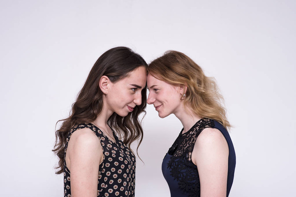 portrait of two beautiful brunette girls and blondes on a white background showing different emotions in different poses. They stand right in front of the camera and look happy - Zdjęcie, obraz