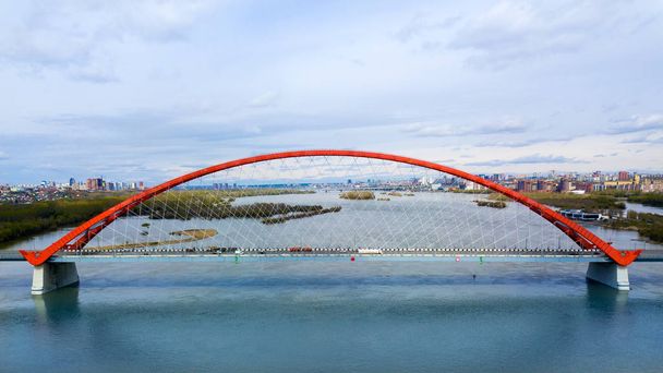 Disparo de helicóptero. Fotografía aérea del gran puente naranja moderno que cruza el río en una megaciudad, un gran parque urbano, modernos edificios de varios pisos
.  - Foto, imagen