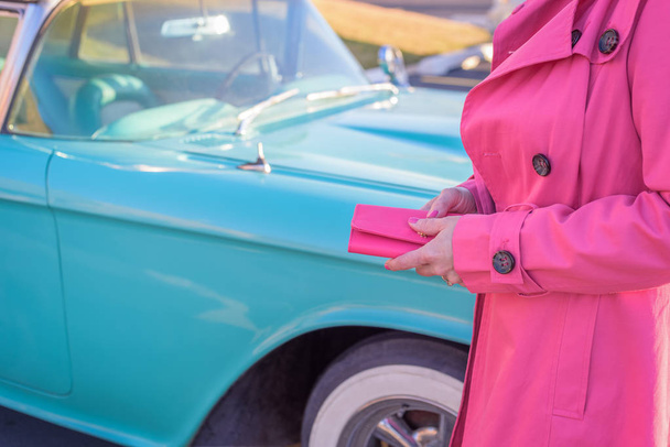 水色の古典的な車を見て財布を保持しているホットのピンクのコートの女 - 写真・画像