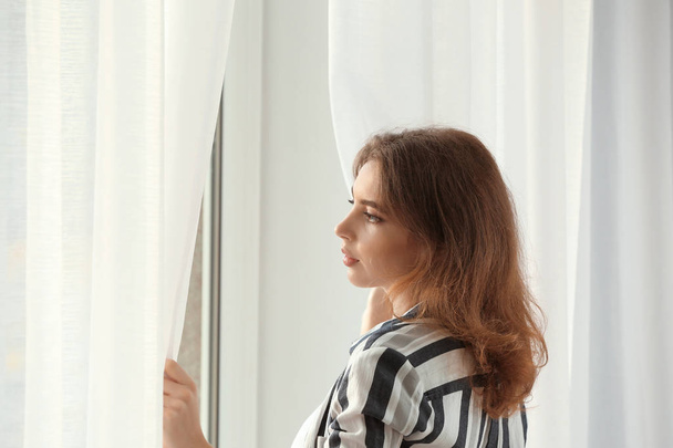 Young woman opening curtains indoors - Fotó, kép