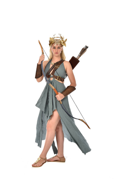 full length portrait of pretty blonde lady wearing fantasy toga gown,  and holding a bow and arrow. standing pose on white background. - Photo, Image
