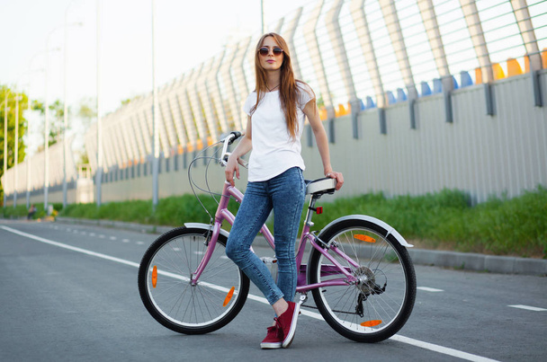 Beautiful woman standing with a bicycle on the road - Фото, изображение