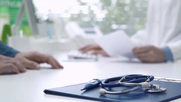 Professional female doctor meeting a patient in the office, she is giving a prescription, stethoscope and medical records on the foreground, healthcare concept - Footage, Video
