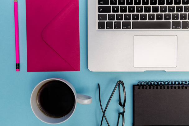 Laptop mit Notizbuch, Brille, Umschlag, Kaffeetasse und Bleistift auf hellblauem Hintergrund - Foto, Bild