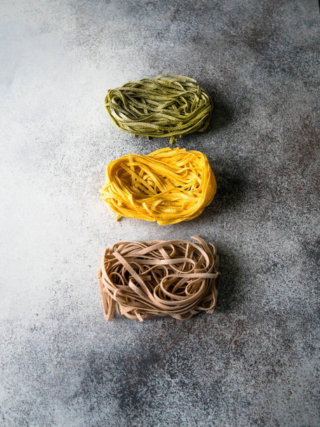 Yellow, green and brown paste or fettuccini on a gray background. Top view - Photo, Image