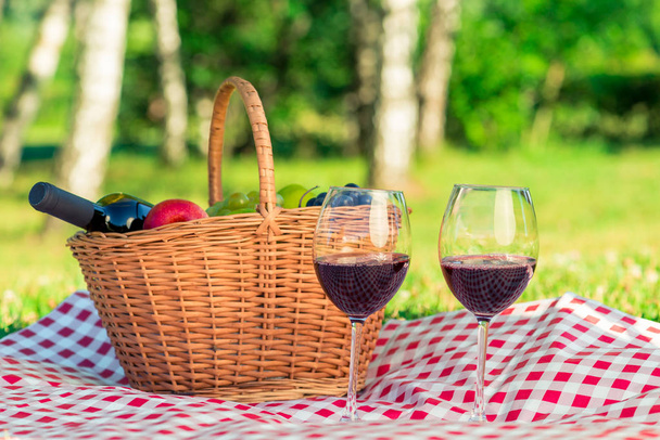кошик з червоним вином і фруктами і двома келихами вина на скатертині на газоні в парку, крупним планом
 - Фото, зображення