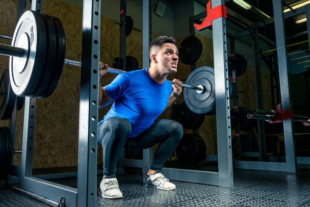 bodybuilder in a blue T-shirt raises a bar weighing 60 kg in the gym - Fotoğraf, Görsel