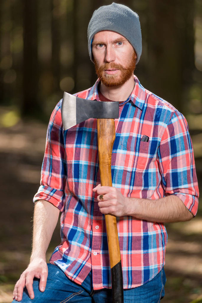 a forester with a red beard posing in a forest with an ax - Foto, Imagen