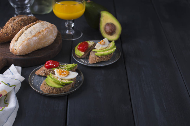 Tasty and juice , sandwich with avocado, tomato and poached egg on wooden chopping board, close up, selective focus. Healthy delicious breakfast or lunch. On a dark background, top x. text - Photo, Image