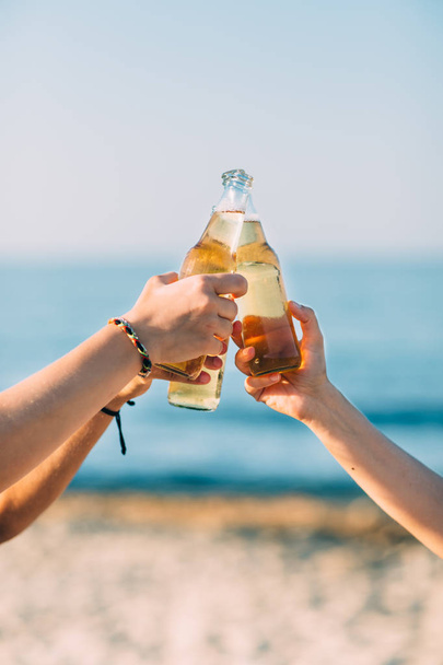 Closeup of hands toasting with bottles of beer at the beach - Foto, afbeelding