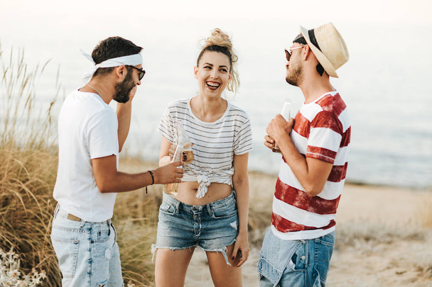 Group of happy young people at the beach talking and drinking beers - Photo, Image