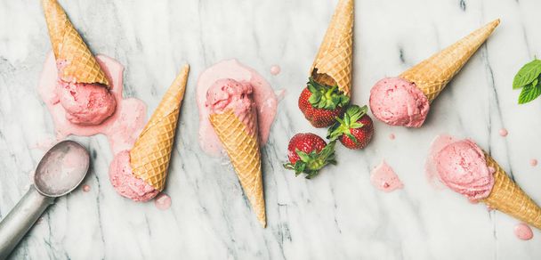 Healthy low calorie summer dessert. omemade yogurt ice cream with strawberries in waffle cones over grey marble background - Fotó, kép
