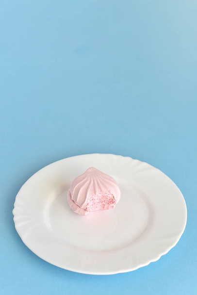 Bitten pink round marshmallow on white plate  - Foto, Bild