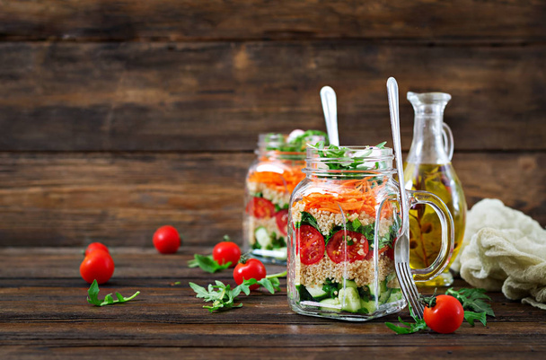 Nahaufnahme von Salaten mit Quinoa, Rucola, Rettich, Tomaten und Gurken in Glasgläsern auf Holzgrund - Foto, Bild